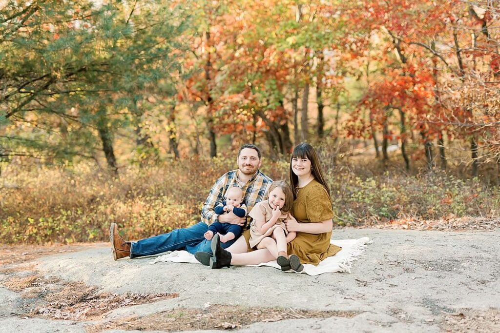 Family of four sitting on rocks in a park, during fall family session in Northern NJ