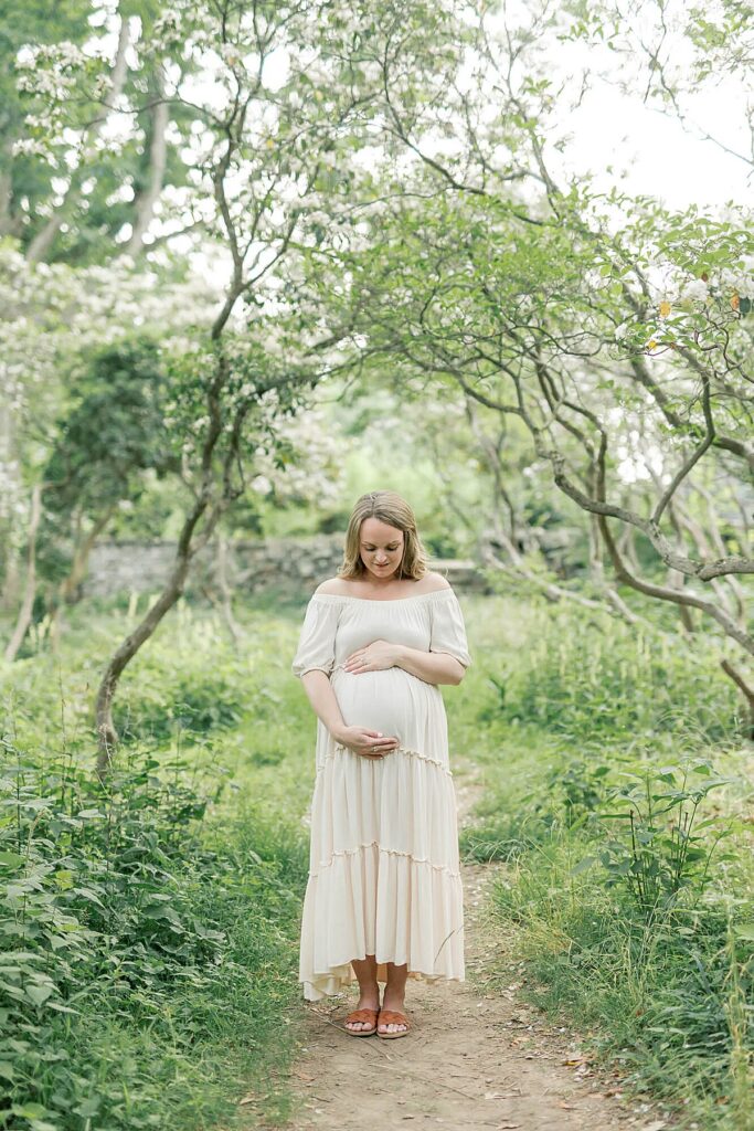 Expectant mother posing in a white dress at Cross Estate Gardens