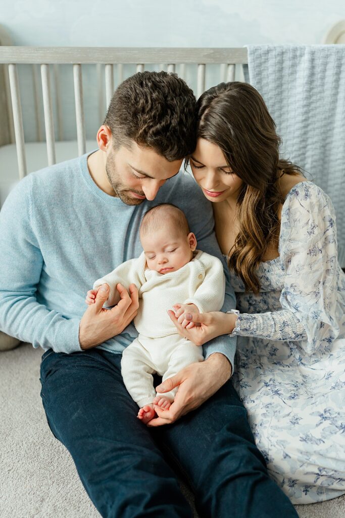 Mother and father cuddling with new baby boy, in front of baby's crib